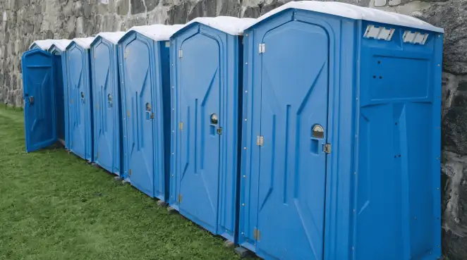 Row of blue portable toilets lined up on grass against a stone wall for event sanitation in Nashua, NH