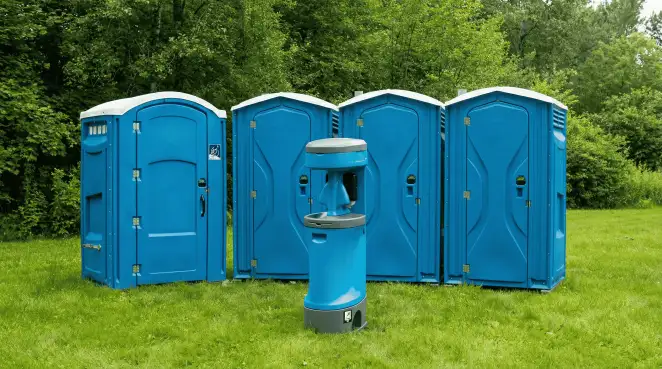 Four blue portable toilets and a matching hand washing station on grass near trees, a common sight at local outdoor events in Nashua, NH